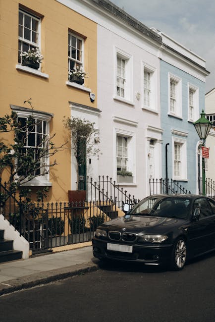 A lively street scene on Portobello Road in Notting Hill, featuring a busy outdoor market with numerous vendors and shoppers. The street is lined with historic brick buildings, some with decorative wh